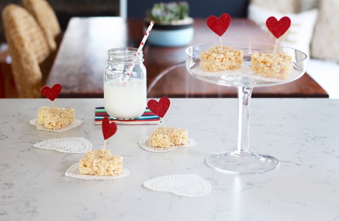 rice krispie valentine heart treats on a white countertop with a glass of milk