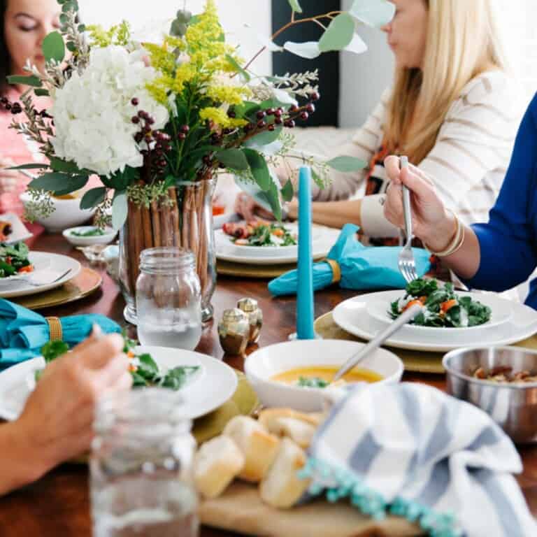 A table full of food at a dinner party. Hands with forks over food eating. Floral centerpiece and candles.